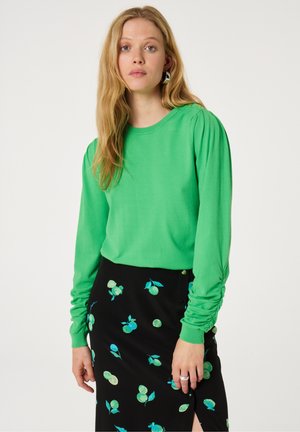 Groene lange mouwen top van zachte stof met geplooide mouwen, gecombineerd met een zwarte rok met kleurrijke fruitprint en een zijsplit.