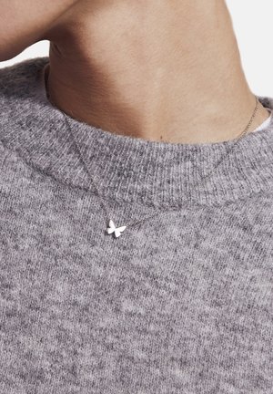 Silver butterfly pendant necklace on a thin chain, worn over a textured gray sweater. The butterfly has a smooth, polished finish.