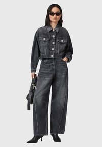 Zwarte denim cropped jacket met bloemenknopen en twee voorzakken, gecombineerd met hoog-getailleerde zwarte wijde jeans en zwarte puntige hakken.