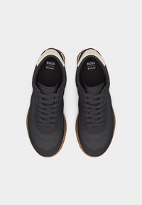 Pereche de adidași casual negri cu șireturi, talpă maro și accente crem, marcați "BOSS" și cu etichetă Ortholite pe interior.