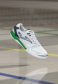 Fehér sportcipő zöld és sötétkék részletekkel, textúrázott hálós felsőrésszel, fűzős dizájnnal és könnyű talppal, amely alkalmas beltéri sportokhoz.