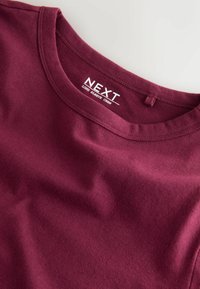 Tricou cu mânecă lungă, de culoare burgundă, cu guler rotund, realizat dintr-un material moale, cu detalii de cusătură vizibile și o etichetă cu inscripția "NEXT LONG SLEEVE CREW".