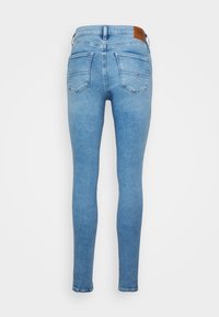 Jeans ajustados de color azul claro con bolsillos traseros y una etiqueta de marca de cuero marrón en la cintura, mostrados desde la parte trasera.