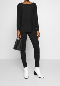 Czarna bluzka z długim rękawem w połączeniu z czarnymi spodniami, białymi botkami za kostkę oraz małą czarną torebką. Strój cechuje się luźnym krojem i gładkimi teksturami.