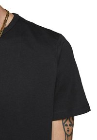 Zwarte katoenen T-shirt met korte mouwen en een ronde hals. Heeft een zachte textuur en zichtbare stiksels aan de rand van de mouw.