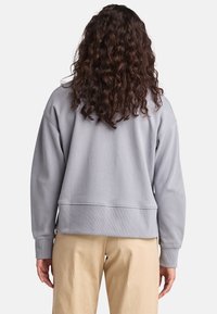 Ljust grå oversized sweatshirt med ribbad muddar och nederkant. Mjuk, texturerad tyg. Synlig sömnad längs kanterna.