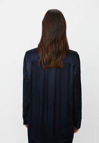 Marineblaue Satin-Hemd mit langen Ärmeln, glatter Textur, geknöpften Manschetten und lockerer Passform, mit einem Rückenpasse und dezentem Glanz.