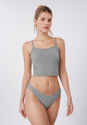 Ung kvinne iført matchende lysegrå kort topp og undertøy, stående mot en enkel hvit bakgrunn.