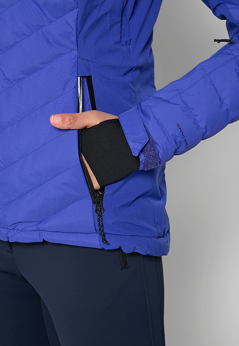 Veste isolée bleue avec un motif matelassé diagonal, poche zippée et poignets élastiques. Présente le logo OMNI-HEAT sur la manche.