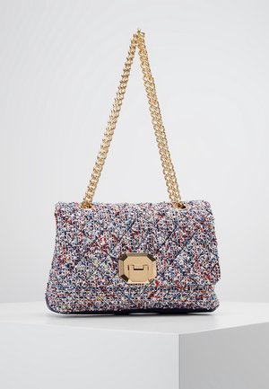 Sac à main en tissu matelassé multicolore avec une chaîne en or et un fermoir géométrique doré, exposé sur un piédestal blanc sur un fond uni.