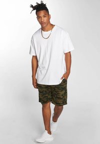 T-shirt bianco in cotone, maniche corte. Pantaloni corti mimetici verdi, fino al ginocchio. Sneakers bianche. Collana semplice in oro. Outfit casual.