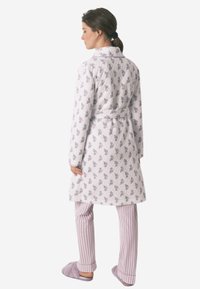 Accappatoio trapuntato con motivo floreale in bianco e viola; presenta una vita con cintura. Abbinato a pantaloni a righe rosa e bianchi e pantofole morbide.