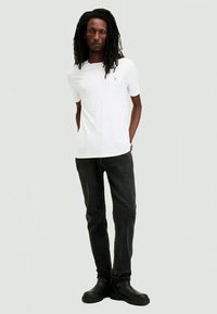 White short-sleeve t-shirt with a v-neck. Black jeans with a straight cut. Black ankle boots. Model poses with hands in pockets.