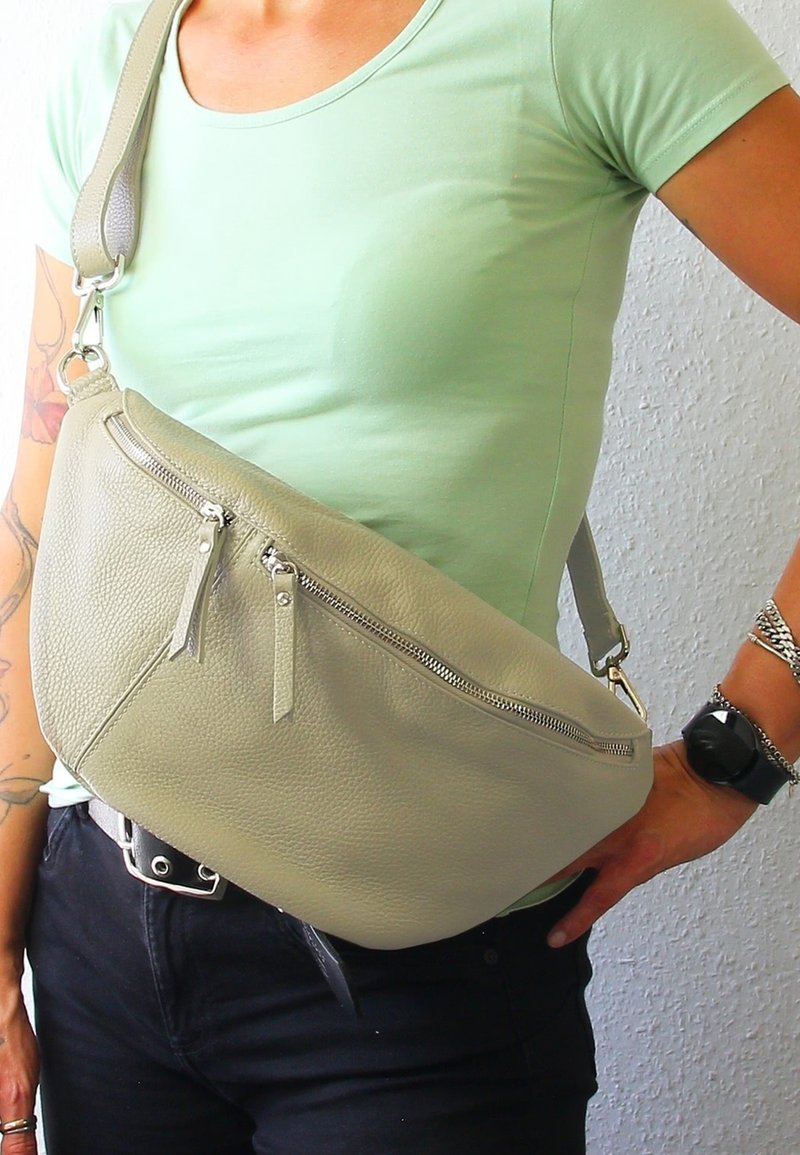 Crossbody tas in zacht, lichtgrijs leer met twee rits](https://plagger.nl/)vakken aan de voorkant, een verstelbare schouderband en een textuurafwerking. Draagt tegen een groene shirt.