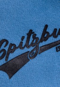 Blue fabric featuring the word "Spitzburg" in black, stylized cursive text with a curved underline, textured surface visible.