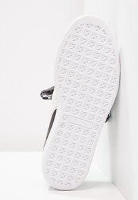 Bílá podešev tenisky Puma směřující vpřed s geometrickým vzorem a viditelným logem, obuv umístěná proti bílým rohovým stěnám.