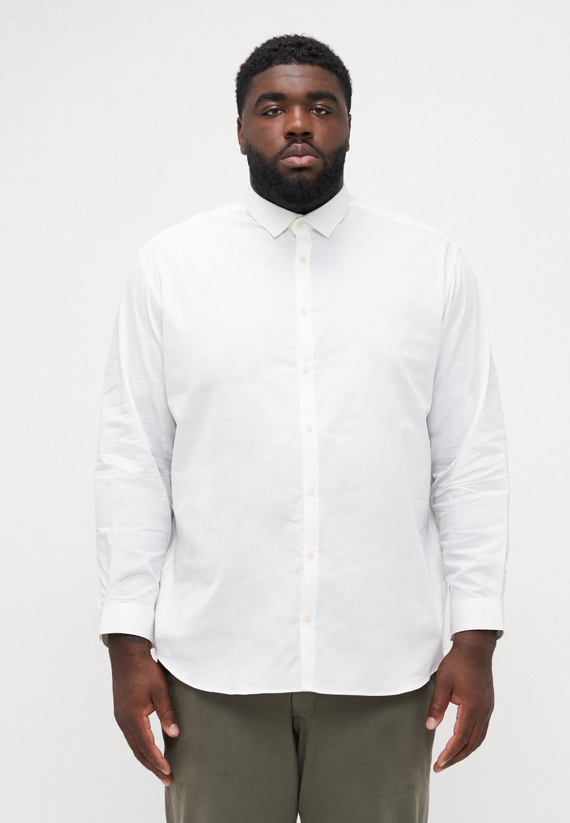 Chemise blanche à manches longues, ornée d'un col, avec une texture lisse et une coupe droite. Les boutons sont de couleur claire, apportant un contraste.