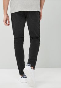 Mustat farkut, joissa on slim fit -malli ja kaksi takataskua, yhdistetty valkoisiin tennareihin. Kankaan pinta on sileä.