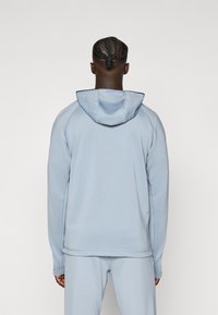 Hoodie bleu clair en tissu lisse. Présente une capuche avec cordon de serrage, des manches longues et des coutures contrastantes le long des coutures.