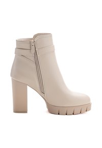 Bota de tobillo beige hecha de material sintético suave, con un alto tacón bloque, cremallera lateral y detalle de cinturón horizontal cerca de la parte superior.