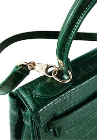 Sac à main en cuir embossé façon crocodile vert foncé avec fermoir doré attachant une bandoulière à la poignée, montrant une texture et des coutures détaillées.