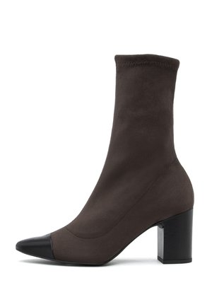 Stivale alla caviglia in suede marrone con un gambale aderente, punta affusolata e una punta in pelle nera a contrasto. Presenta un tacco a blocco per maggiore stabilità.
