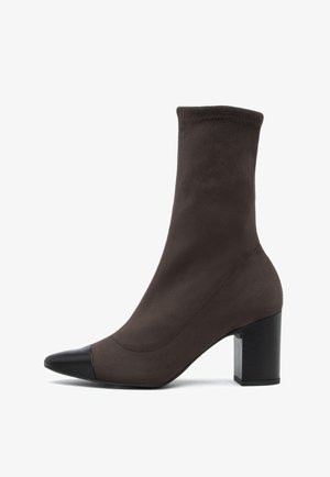 Rudos zomšiniai kulkšniniai botai su prigludusia aulu, smailiu ratu ir kontrastinga juoda odine kepure. Suvartas blokinis kulnas užtikrina stabilumą.