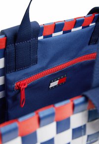 Red, white, and blue woven tote bag with a top handle, featuring an external red zipper pocket and a logo patch on the interior.