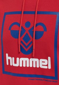 Röd huvtröja med en blå logotyp som har en grafisk design och vit text "hummel." Dragkedjorna är också röda. Mjuk bomullsmaterial.