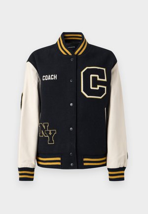 Granatowa kurtka typu varsity z wełny z kremowymi skórzanymi rękawami, ozdobiona żółtymi paskami, haftowanymi naszywkami "C" i "NY" oraz logo "COACH".