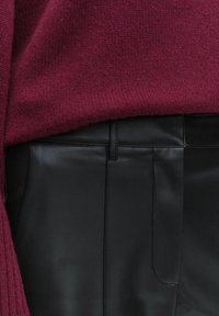 Punainen neulepaita yhdistettynä mustiin nahkahousuihin. Neulepaidassa on ribaatut pinnat, kun taas housuissa on sileä pinta ja taskut.