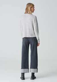 Hellgrauer, strukturierter Pullover mit lässigem Schnitt, kombiniert mit hoch sitzenden, dunkelgrauen weit geschnittenen Jeans mit umgeschlagenen Säumen. Schwarze Stiefeletten.