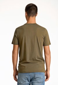 Camiseta de manga corta en verde oliva con un cuello redondo y textura suave, combinada con unos vaqueros de mezclilla azul, vista desde atrás.