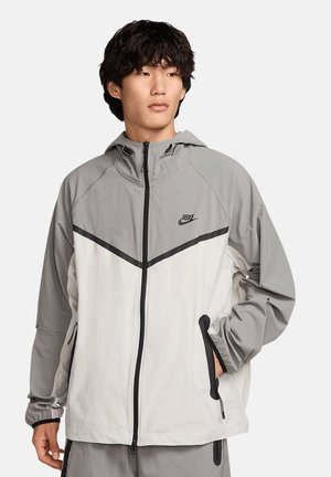 Nike jacket featuring a gray and white color scheme, lightweight fabric, zip closure, adjustable hood, and contrasting accents along seams.