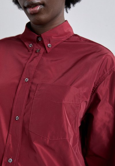 Red button-up shirt made from a glossy material, featuring a pointed collar, chest pocket, and matching buttons along the front.