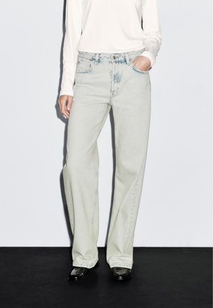 Jeans a gamba larga in denim con una finitura sbiadita, di un lavaggio chiaro. Presentano cinque tasche e una chiusura con bottone anteriore. Abbinati a una maglietta a maniche lunghe.