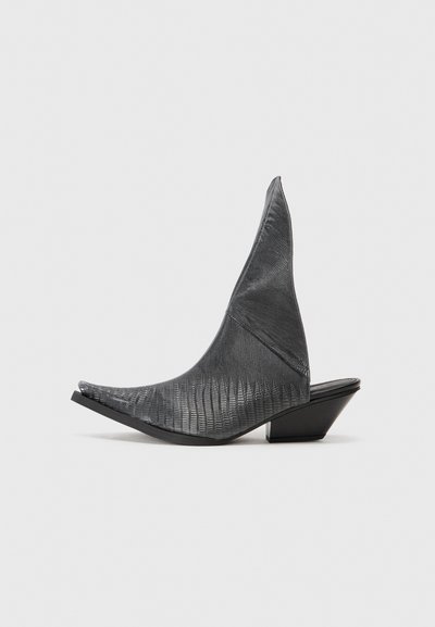 Black heeled mules with a pointed toe and a textured snake-skin pattern. Features a low, triangular heel and a smooth, curved upper design.