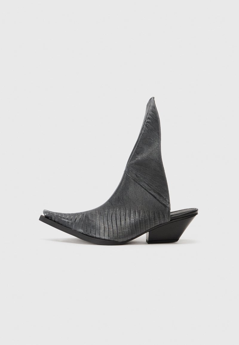 Mule-uri negre cu toc înalt, cu vârful ascuțit și un model texturat de piele de șarpe. Dispune de un toc jos, triangular și un design al partea superioare neted și curbat.