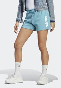 Ljust blå bomullsshorts med elastisk midja, vit "adidas"-logga, ihop med vita strumpor och skor samt en jeansjacka.
