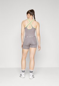 Top sportiv gri, cu bretele încrucișate și accente galbene neon, asortat cu pantaloni scurți gri. Adidași albi și șosete cu dungi.