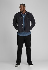 Dark denim jacket with silver buttons, paired with a blue polo featuring a striped collar, black pants, and black sneakers.