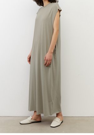 Lichtgrijze, mouwloze maxidress met een ronde halslijn, zachte textuur, zijzakken en een losse pasvorm, gecombineerd met witte instap schoenen.
