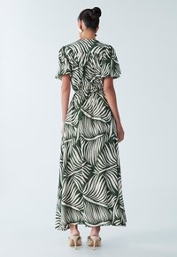 Roheline maksikleit valge lehisemustriga, lühikeste puffervarrukatega, vöökoht kitsendatud ja voolava seelikuga; kantud mustriliste kõrgete kontsadega.