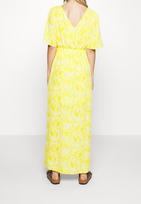 Robe maxi jaune vif avec motif floral, dos en V, manches courtes, taille cintrée, et associée à des sandales espadrilles marron.