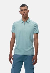 Lys blå polo skjorte med korte ermer, glidelås foran og teksturert stoff. Har minimale sømdetaljer nær skulderen.