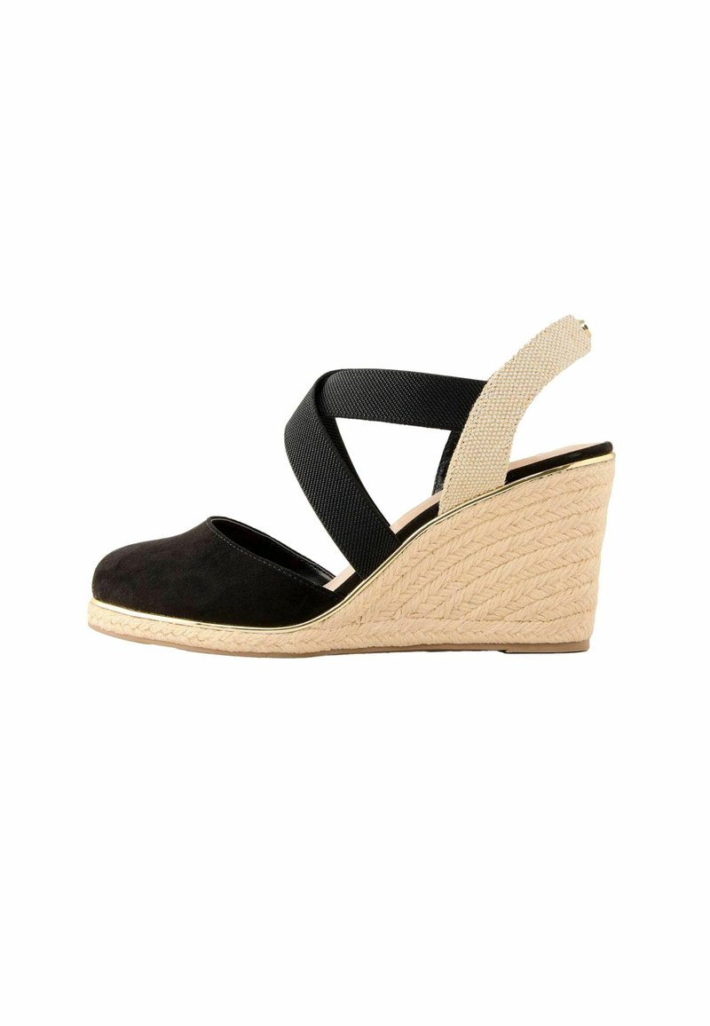 Zapato de cuña de ante negro con suela de yute trenzado, que presenta correas elásticas entrecruzadas en negro y beige claro. Textura suave y puntera redondeada.