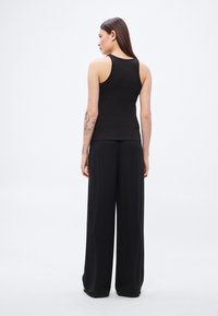 Μαύρο αμάνικο τοπ με εφαρμοστή σχεδίαση συνδυασμένο με μαύρο παντελόνι φαρδιάς γραμμής, και τα δύο από απαλό ύφασμα με ελάχιστες λεπτομέρειες.