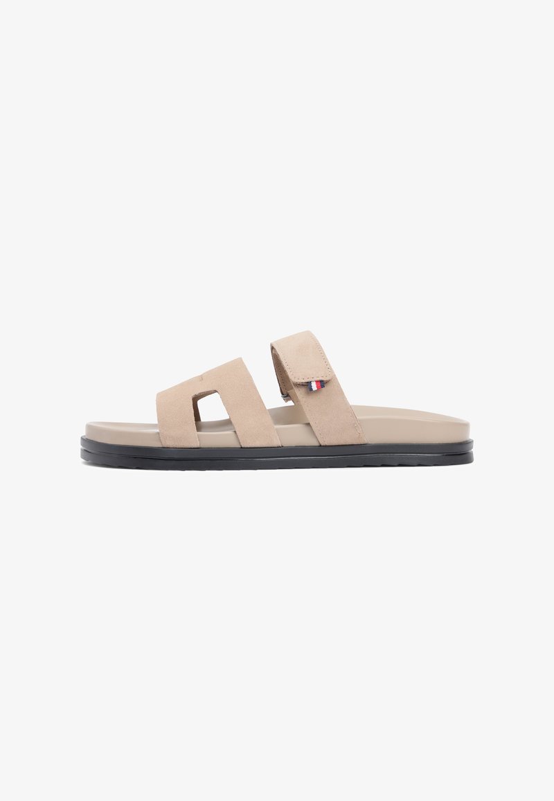 Μπεζ σανδάλια slide από σουέντ με δύο ρυθμιζόμενα λουριά, επίπεδη ανοιχτό μπεζ σόλα και μαύρη λαστιχένια εξωτερική σόλα για καλύτερη πρόσφυση. Διακοσμημένα με λογότυπο.