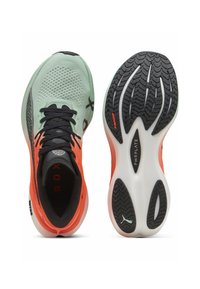Zapatillas deportivas ligeras con parte superior de malla en verde menta, acentos en negro y naranja, suela exterior de goma texturizada en negro y media suela acolchada.