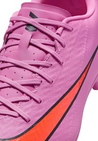 Rosa fotbollssko med texturerad syntetisk ovandel, svarta accenter och ett orange band. Har snörningsdesign och spetsig tå.